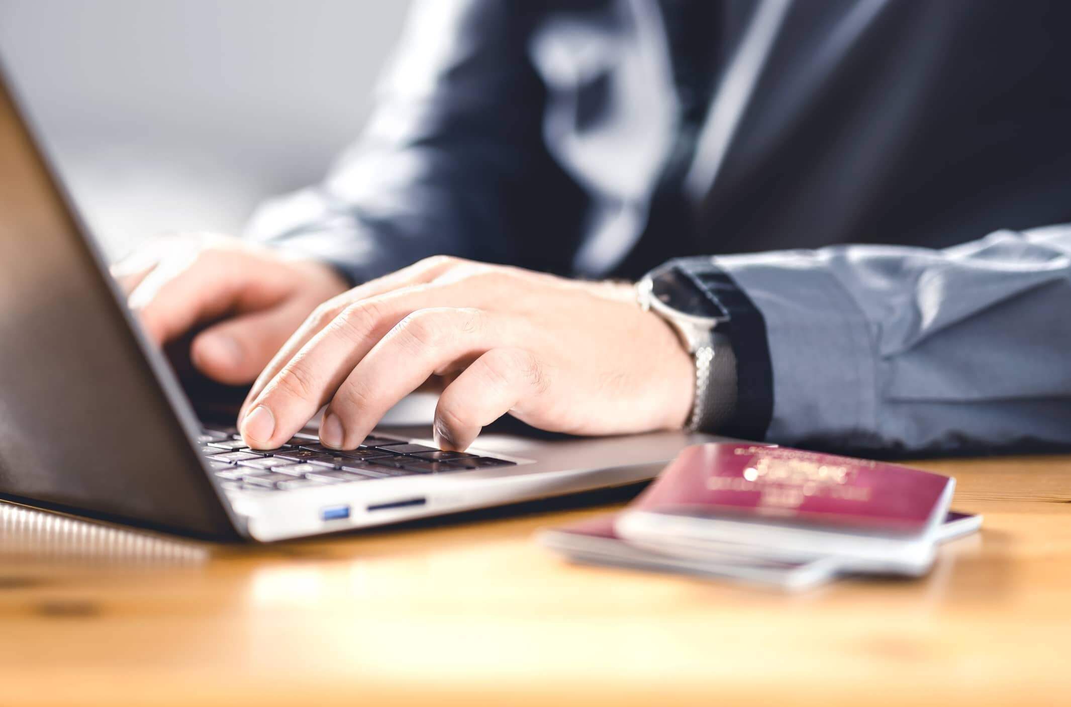 A person sitting at a desk with a laptop computer and a passport open in front of them.