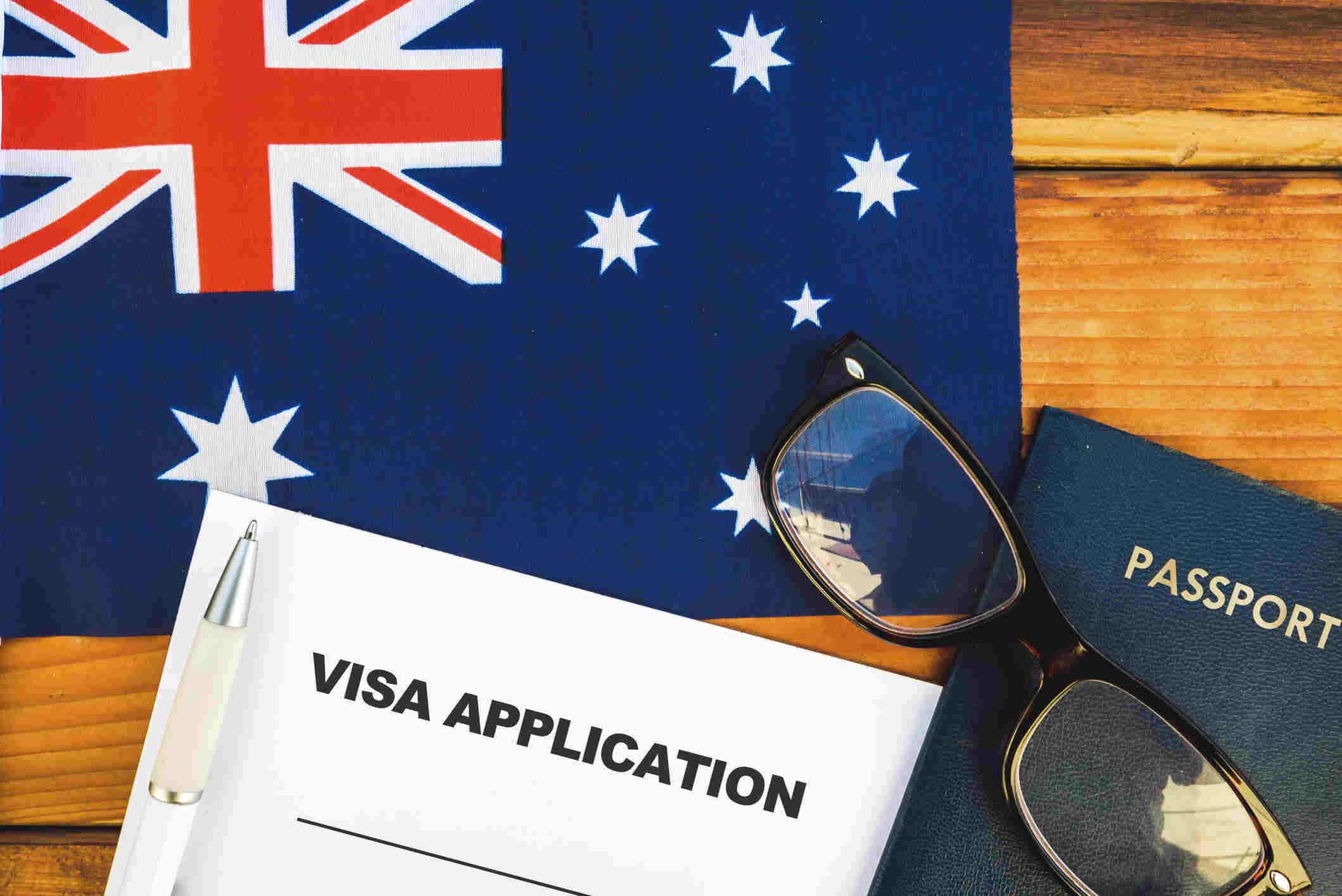 Travel documents for an Australian visa application, including a completed form, passport, and pen.