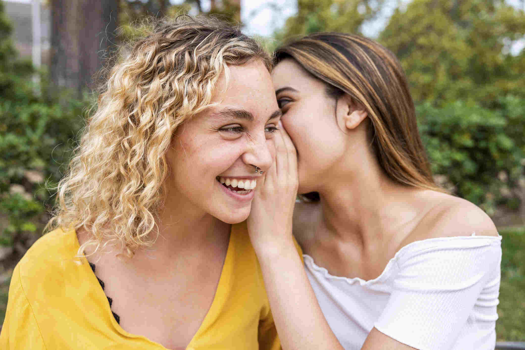 A young woman whispering a secret to her friend in a park