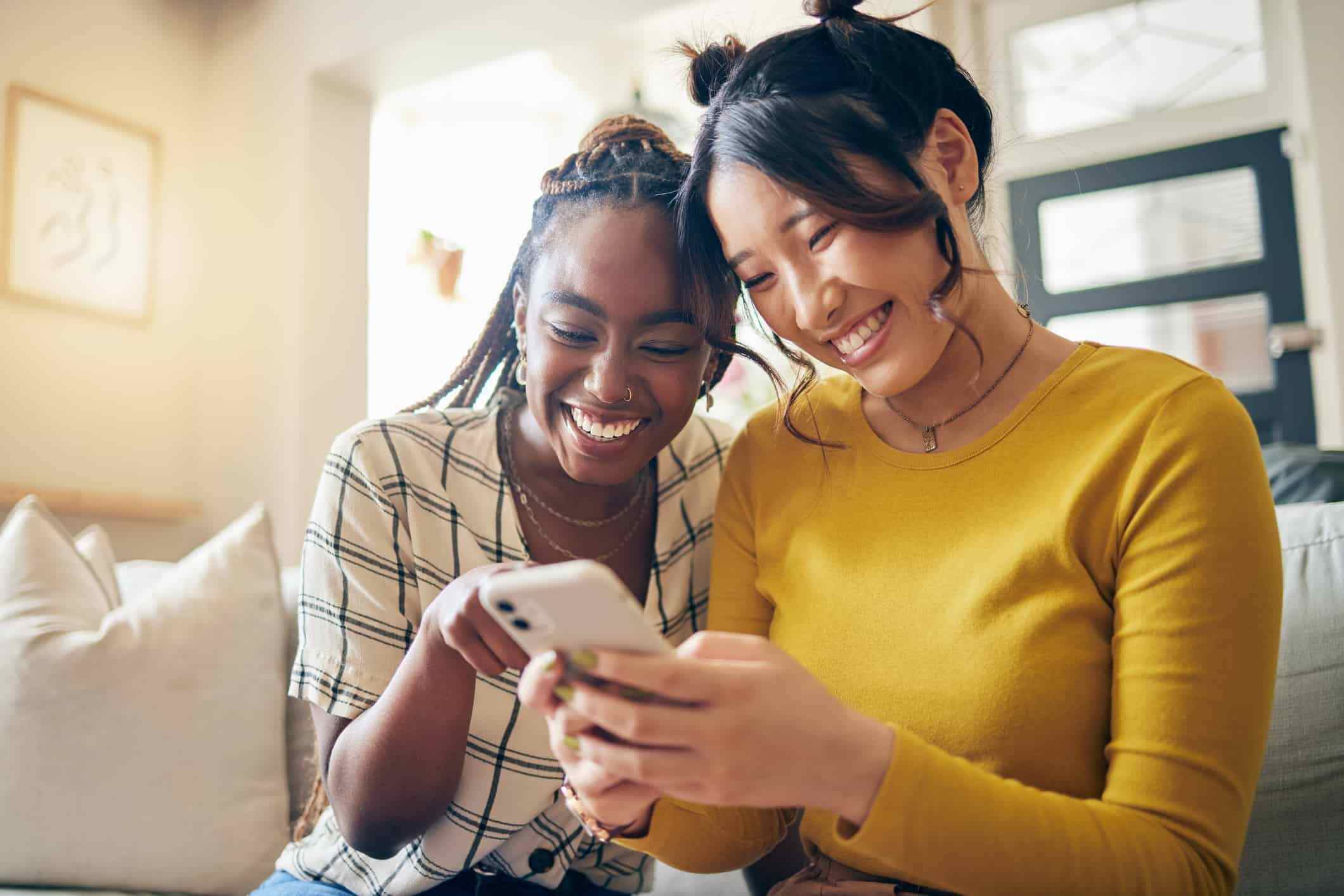 A group of people sitting on a couch, looking at their phones and laughing.