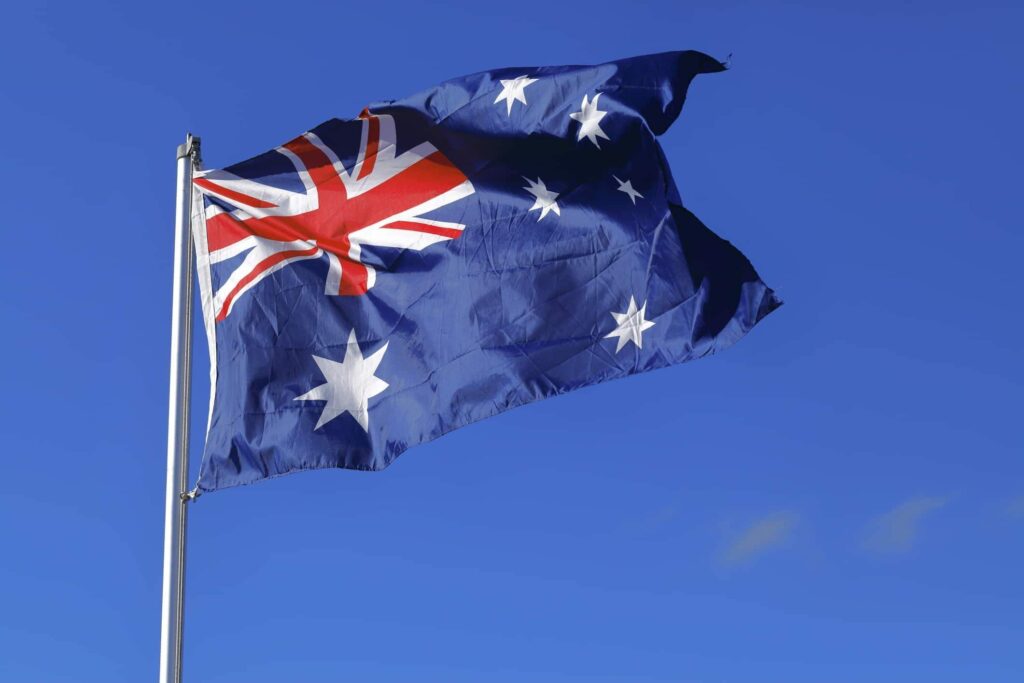 Australian flag with the Union Jack in the top left corner and seven white stars on a blue field, waving in the wind against a clear blue sky